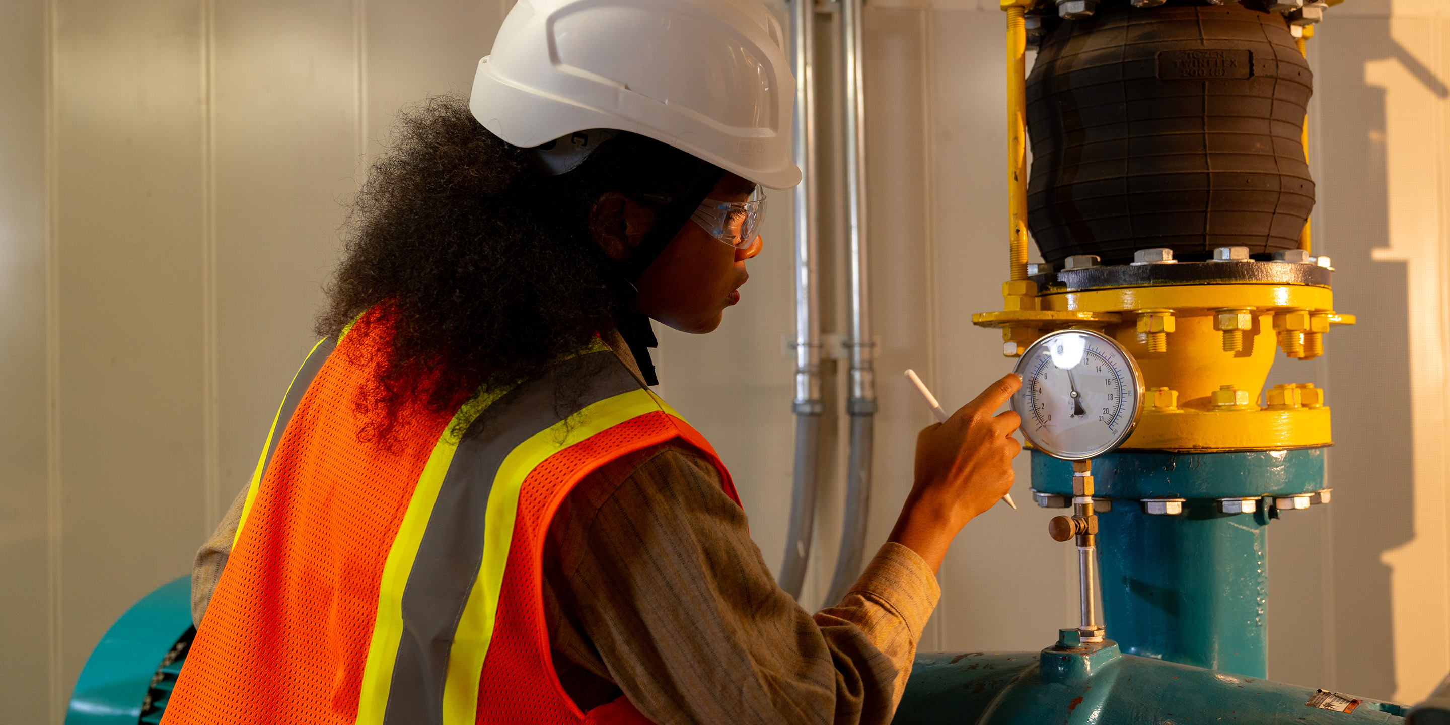 A worker in a safety vest checks a pressure gauge on a large valve in an industrial setting, ensuring operational efficiency and safety.