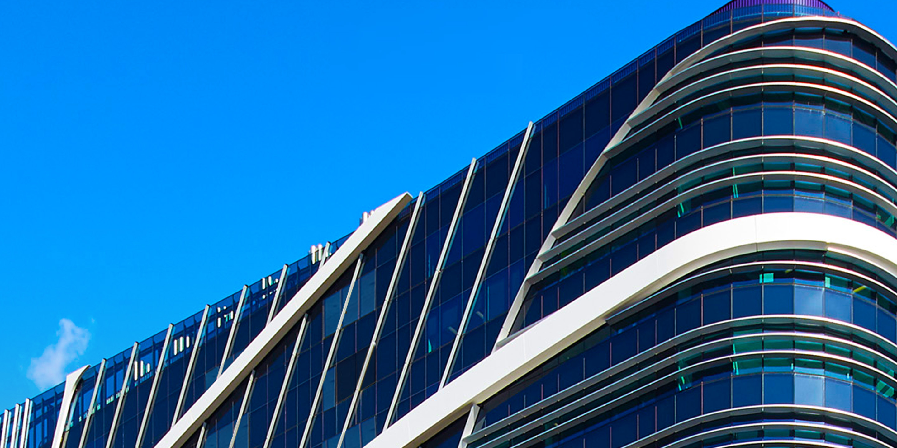 Discover the stunning design of a contemporary building with sleek lines, glass facades, and unique geometric patterns set against a vibrant blue sky.