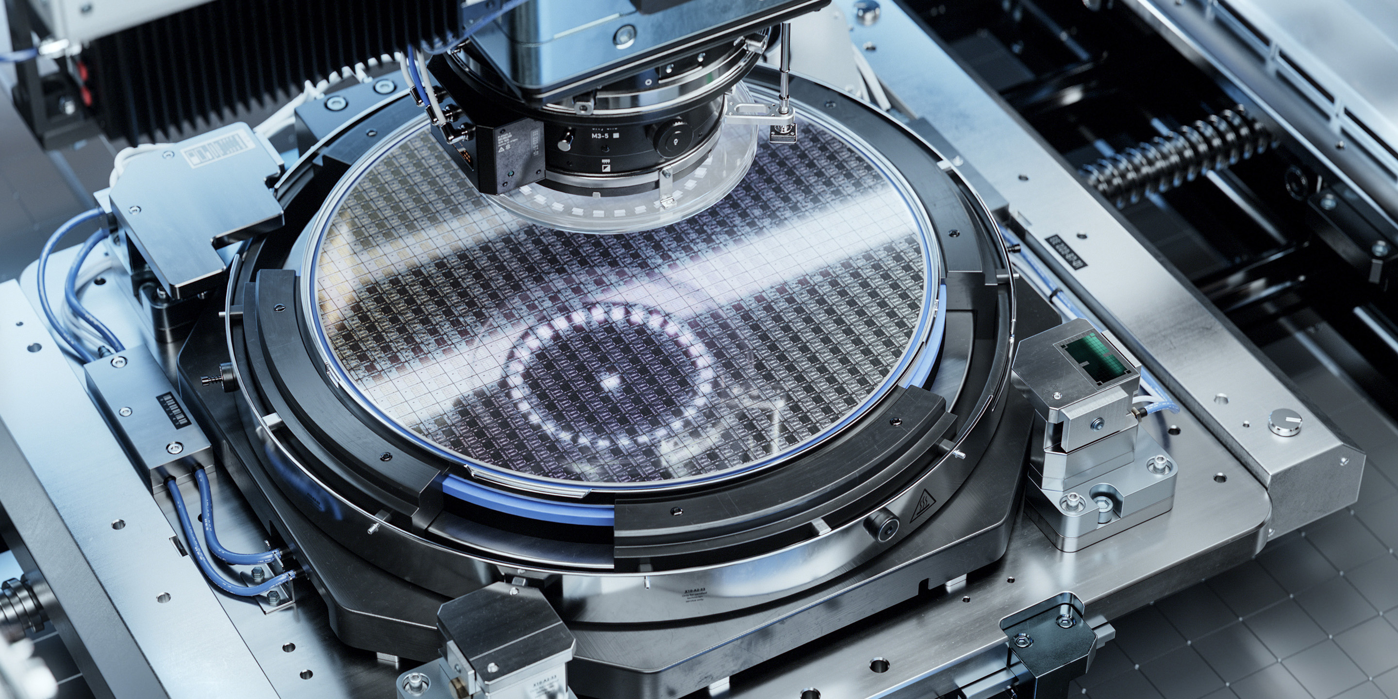 Close-up view of a semiconductor wafer being processed on advanced machinery, highlighting intricate patterns and precision engineering in a clean room environment.