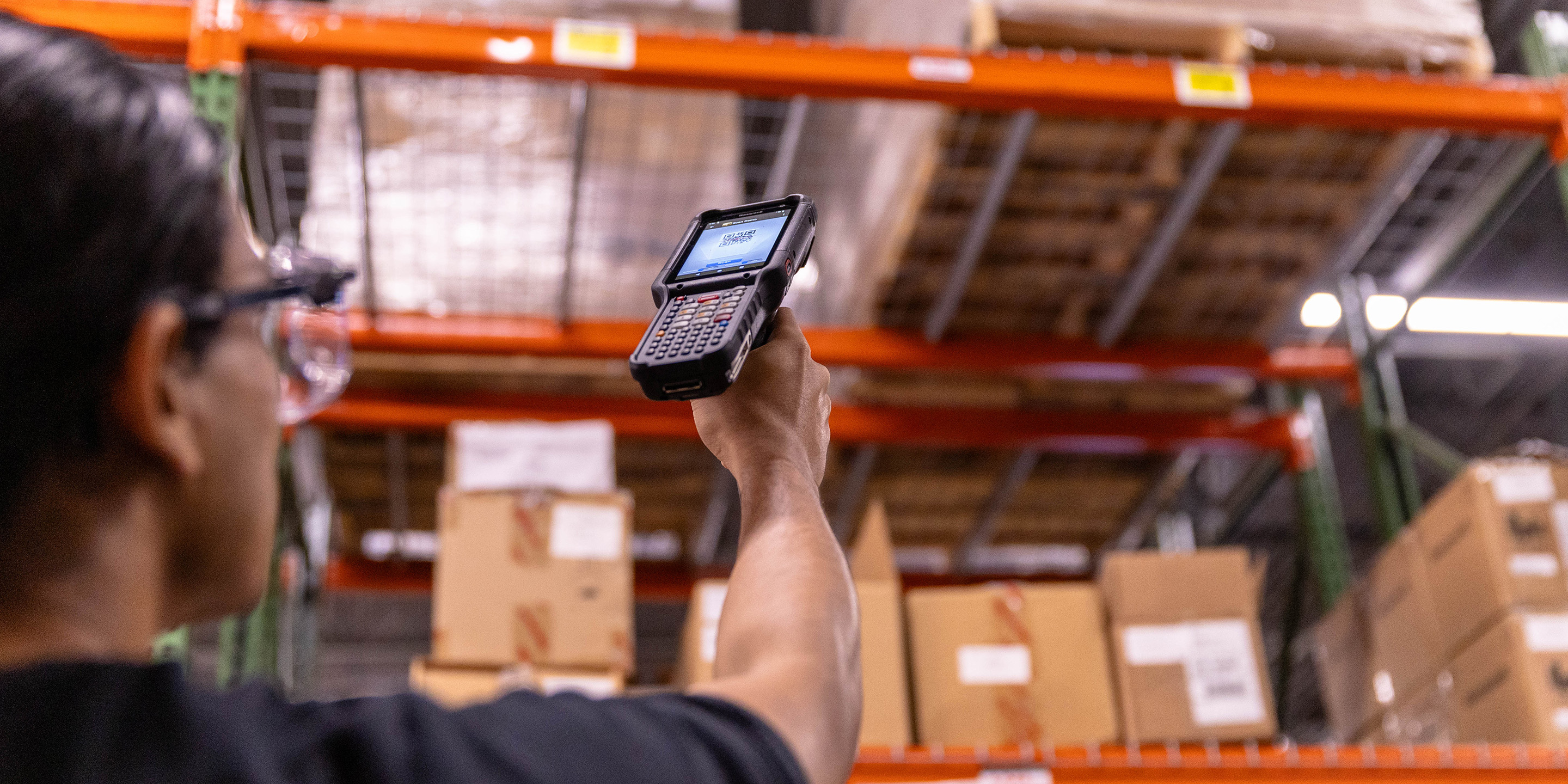 A warehouse worker uses a handheld barcode scanner to manage inventory efficiently in a busy storage environment. Perfect for enhancing supply chain operations.